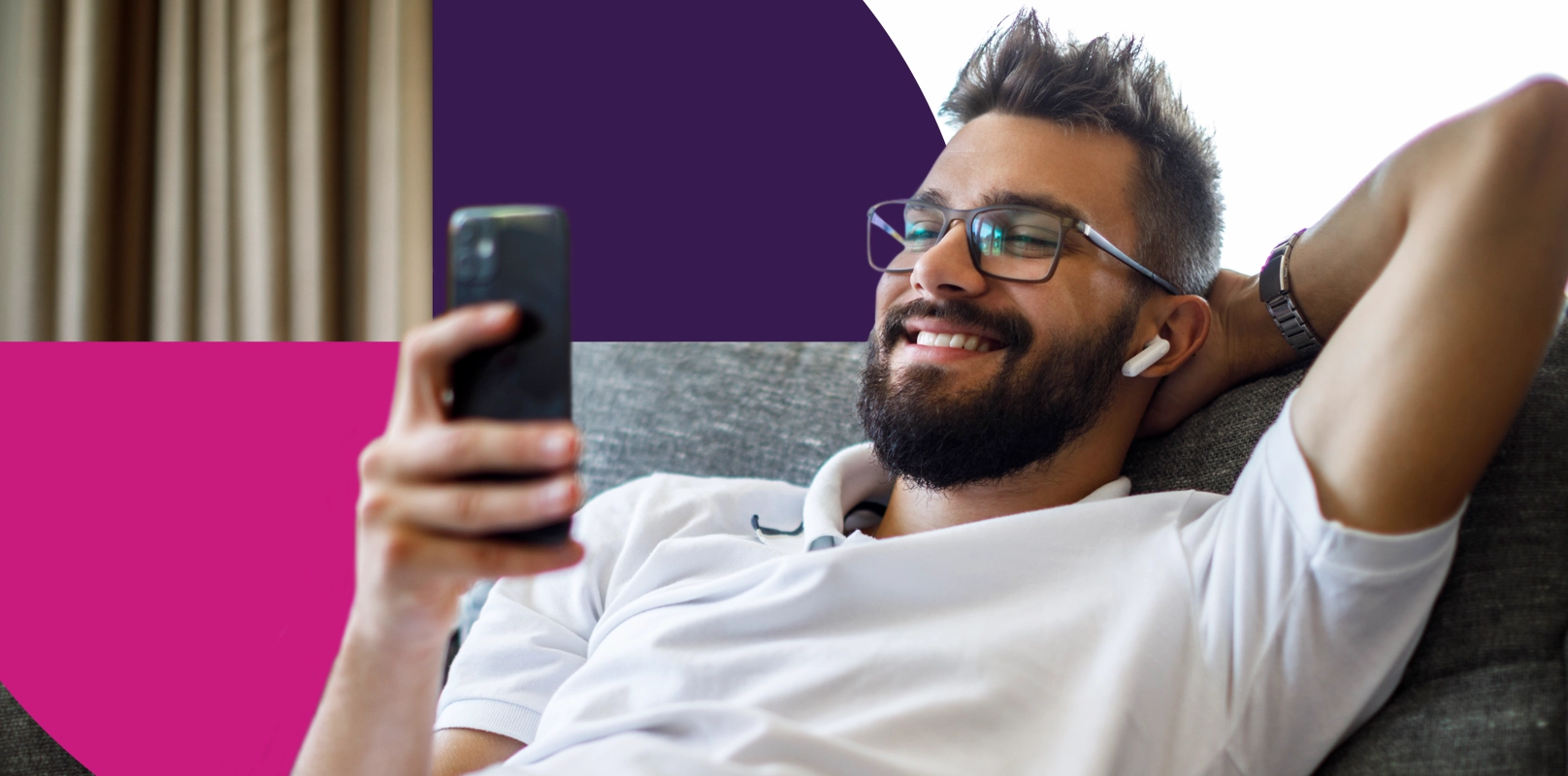 Smiling young man with Bluetooth headphones using smart phone on sofa to access his High Interest Savings Account (HISA) on the Saven Financial app.